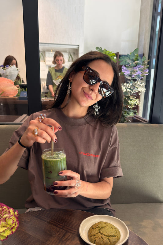 Woman wearing Limited Edition CR T-shirt mocha oversized graphic tee at cafe with matcha - Corazon Roto