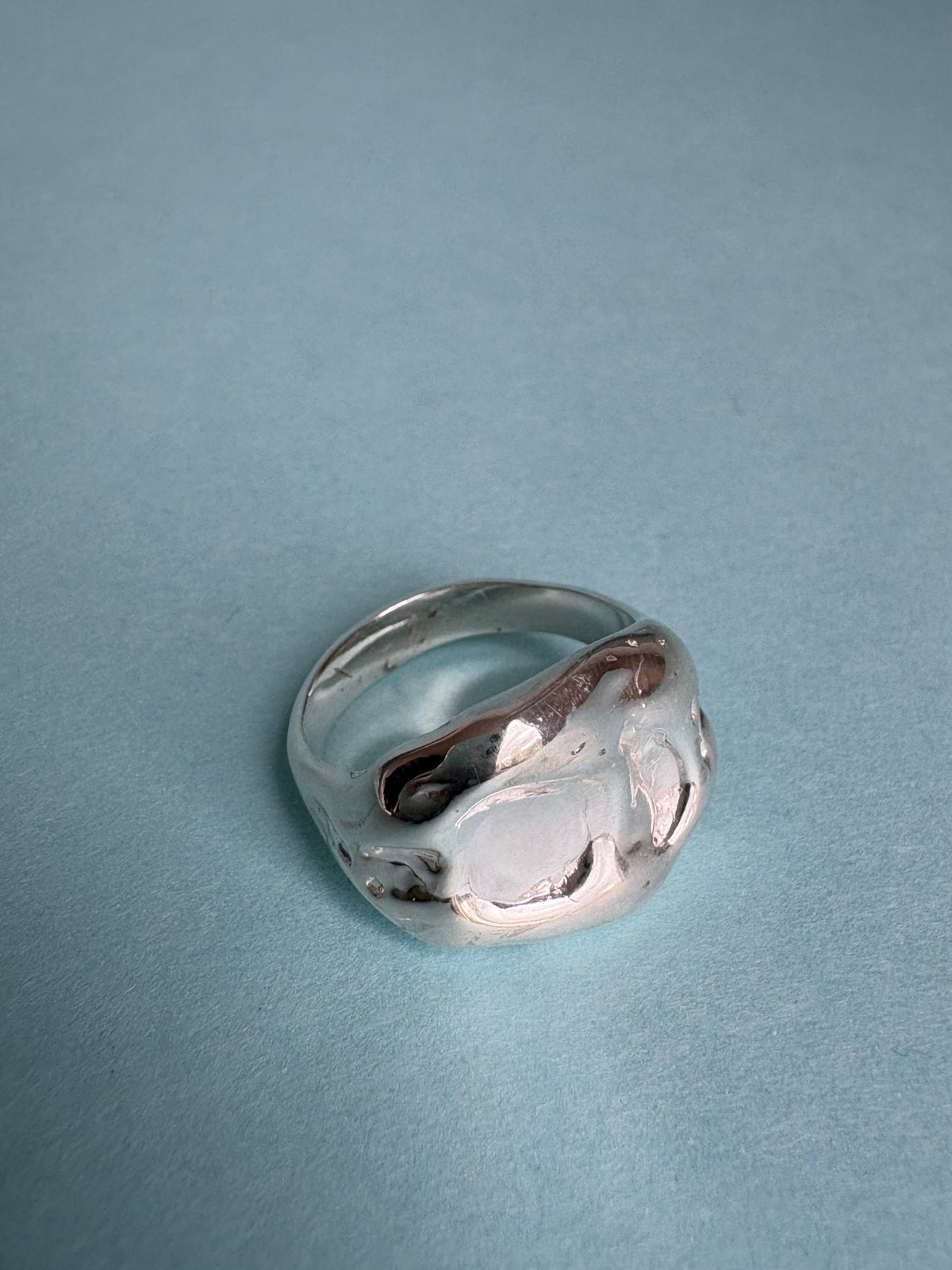 STUDIO MUREA Chunky Ring, a wide rippled silver band, on a pale blue background