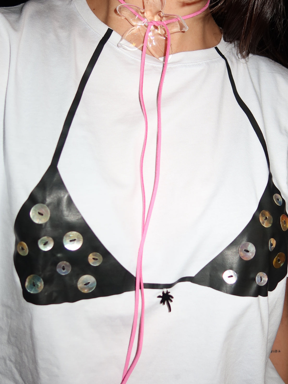 Close-up of the Nacar print: a black bikini top hand-finished with mother-of-pearl buttons and a pink cord