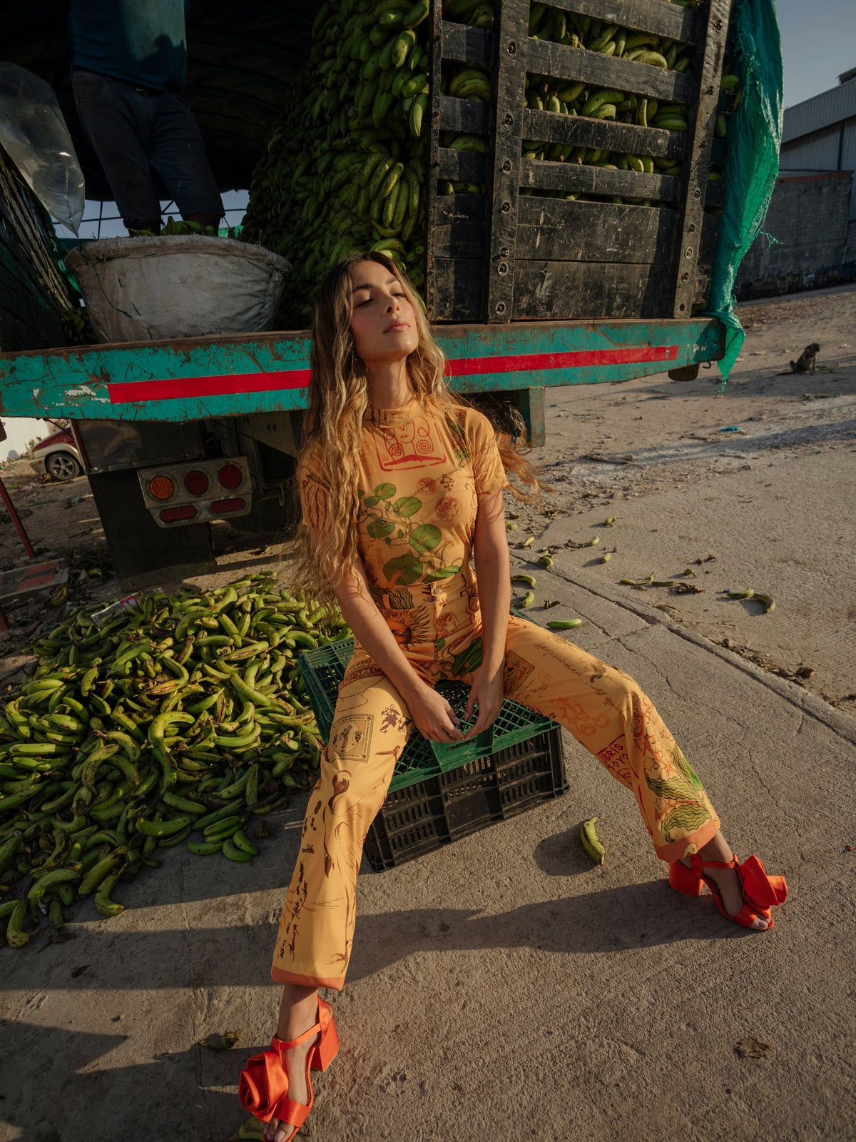 Circe Trofo printed set worn seated on crates among green bananas, with red heels