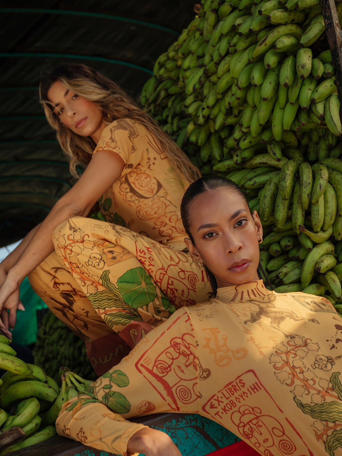 Two models in the Circe Trofo ochre printed set among crates of green bananas