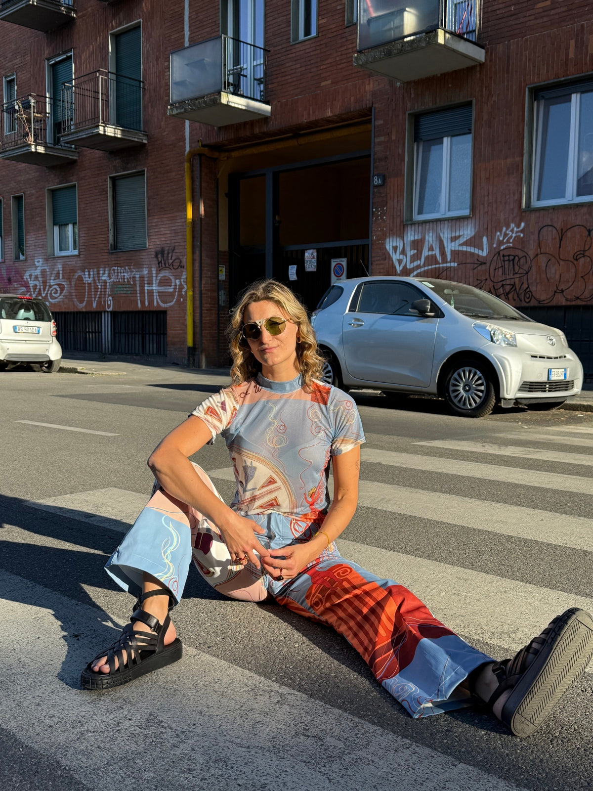 Model in the Circe Moiras printed set seated on a pedestrian crossing in a city street