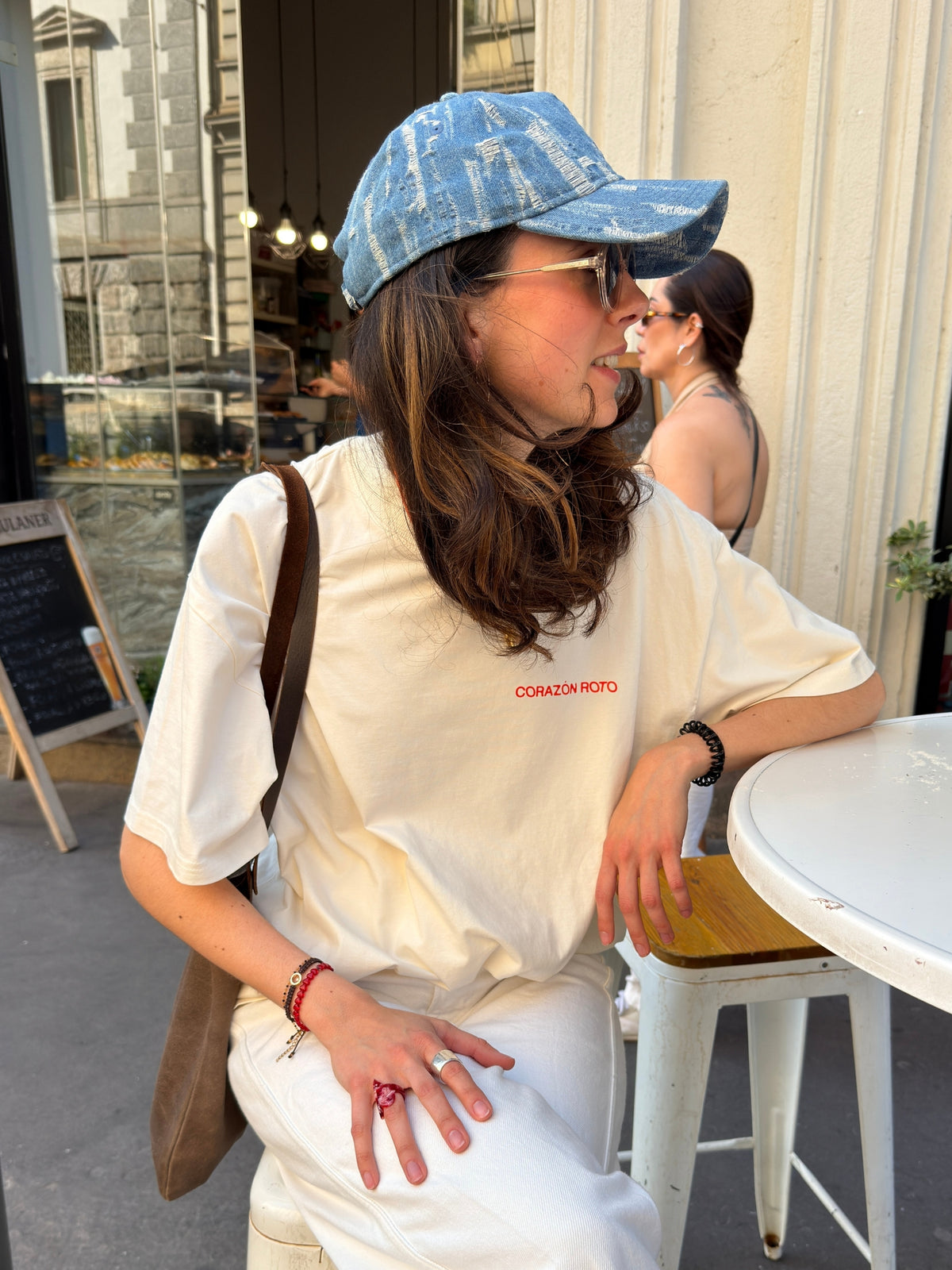 Model wearing the cream Limited Edition CR T-shirt by Corazon Roto at a cafe table