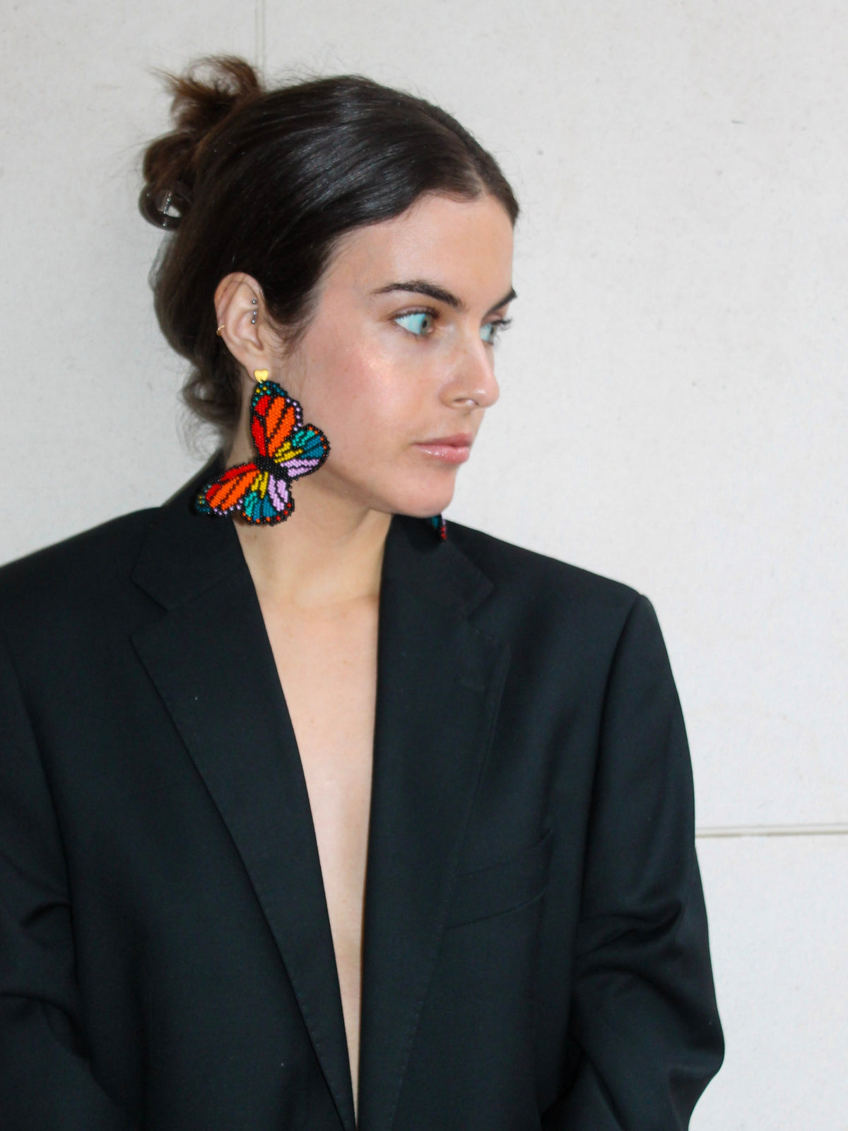 Mariposa butterfly earrings by Dearly worn with a black blazer against a white wall