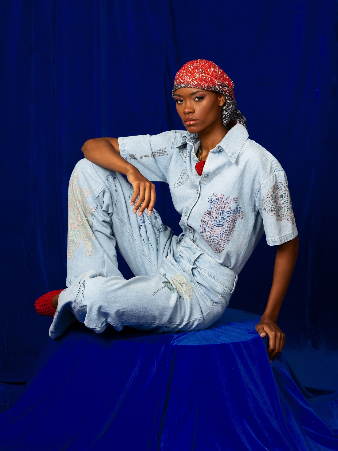 Model seated in the MACONDIA crystal-embellished light denim set against a blue backdrop