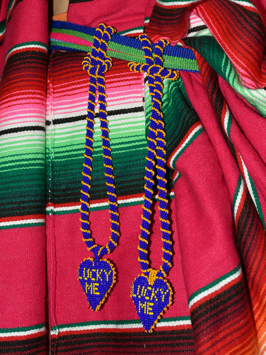 Two Lucky Me beaded heart necklaces by Pajara Pinta laid on a striped woven blanket