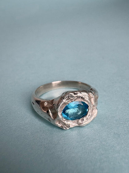 STUDIO MUREA Azul Profundo Ring, a blue topaz in a molten-look silver setting, on a pale blue background