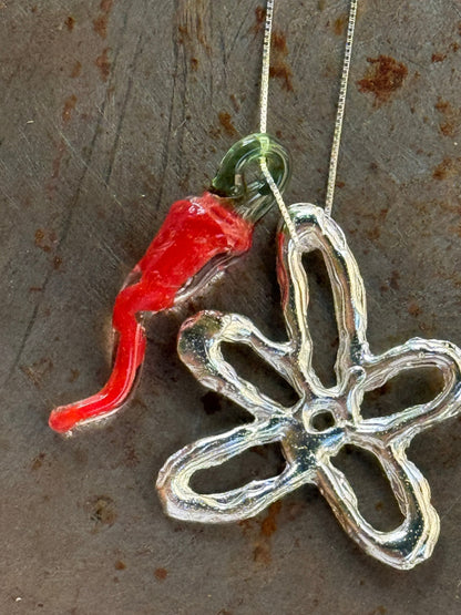 Glass chilli and flower charms of the VOLD Mini Charm Necklace on stone