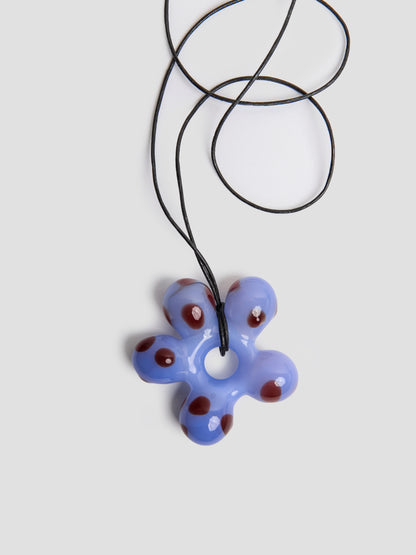 Close view of the handmade blue glass flower charm by VOLD on its black leather cord