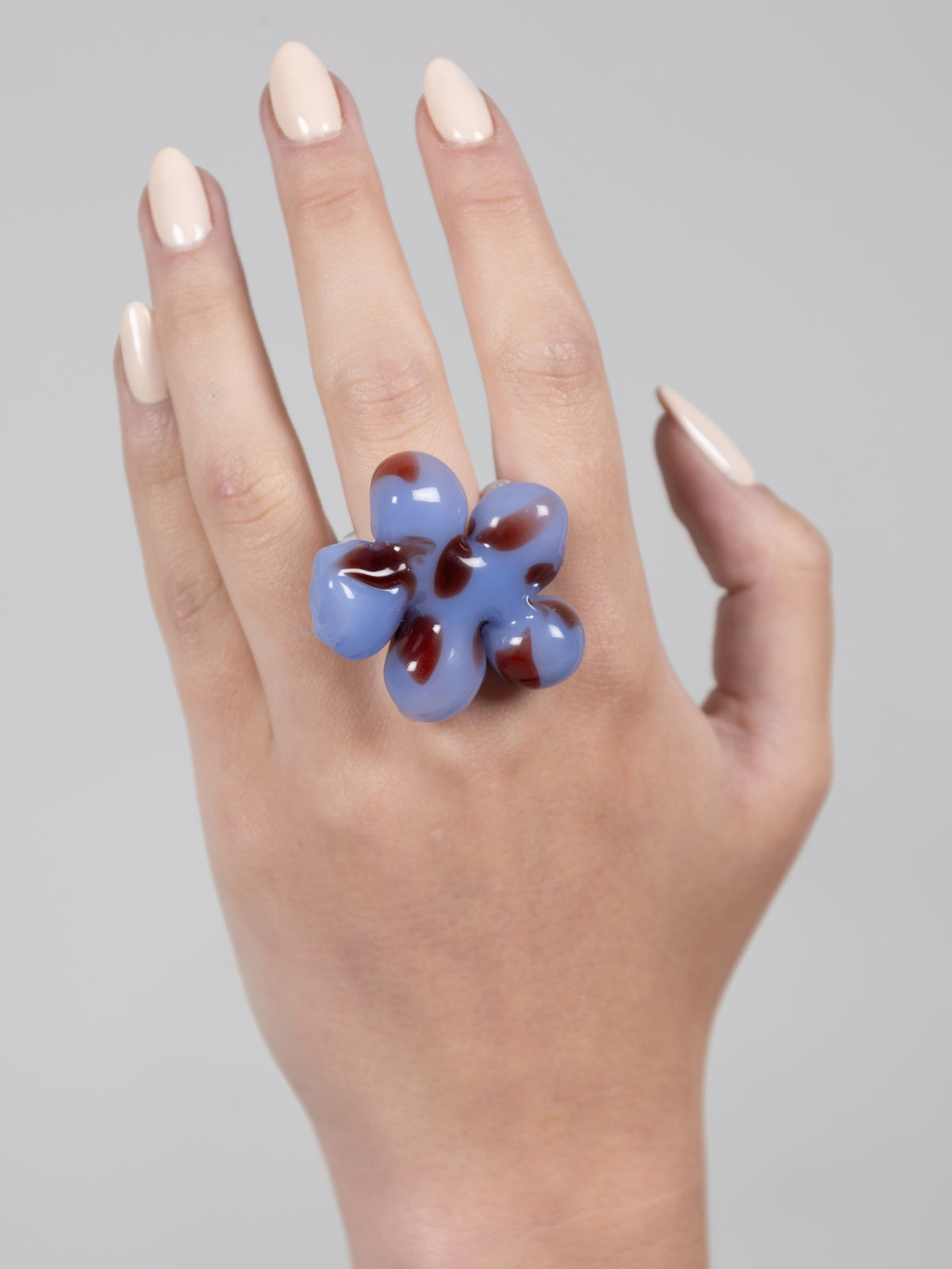 Paradise Maxi Flower Ring by VOLD: a chunky light blue glass flower with burgundy markings worn on a hand